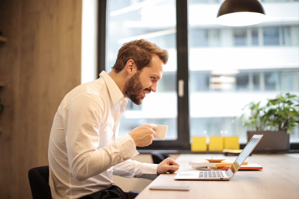 man service telemedicine man holding teacup in front of laptop on top of table inside the room